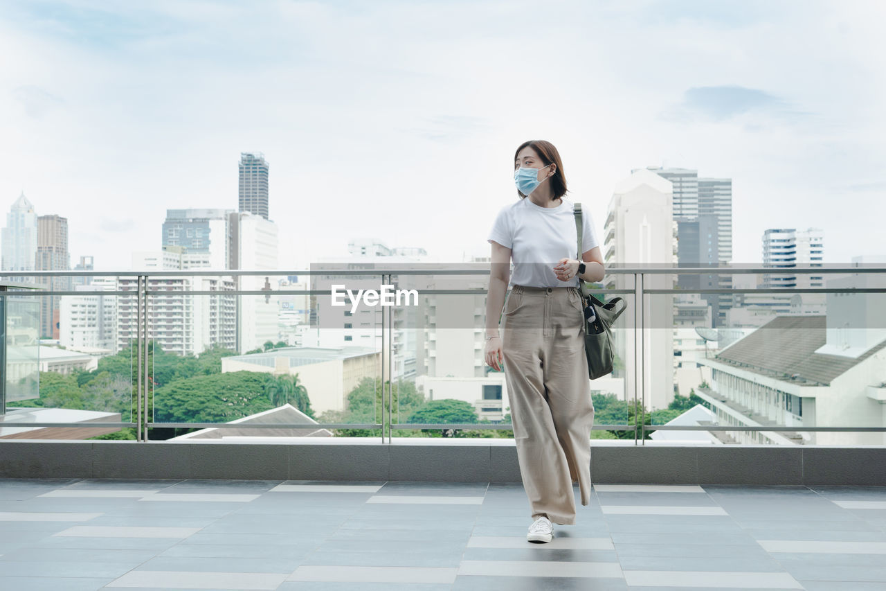 Solo asian woman wear protective mask during outdoor break and relax at rooftop with city background