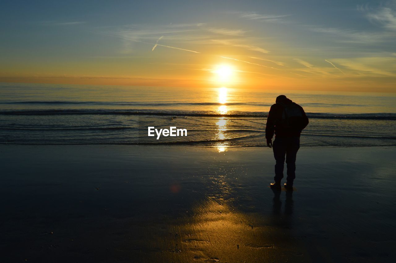 View of person standing on beach at sunset