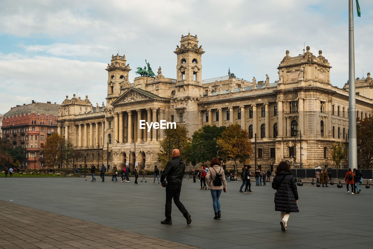 GROUP OF PEOPLE IN FRONT OF HISTORICAL BUILDING AGAINST CLOUDY SKY