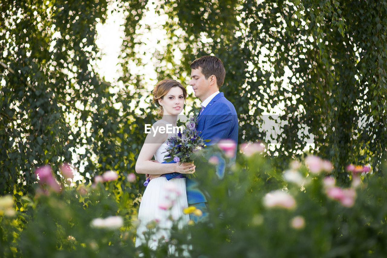 Side view of newlywed couple standing on grassy field at park