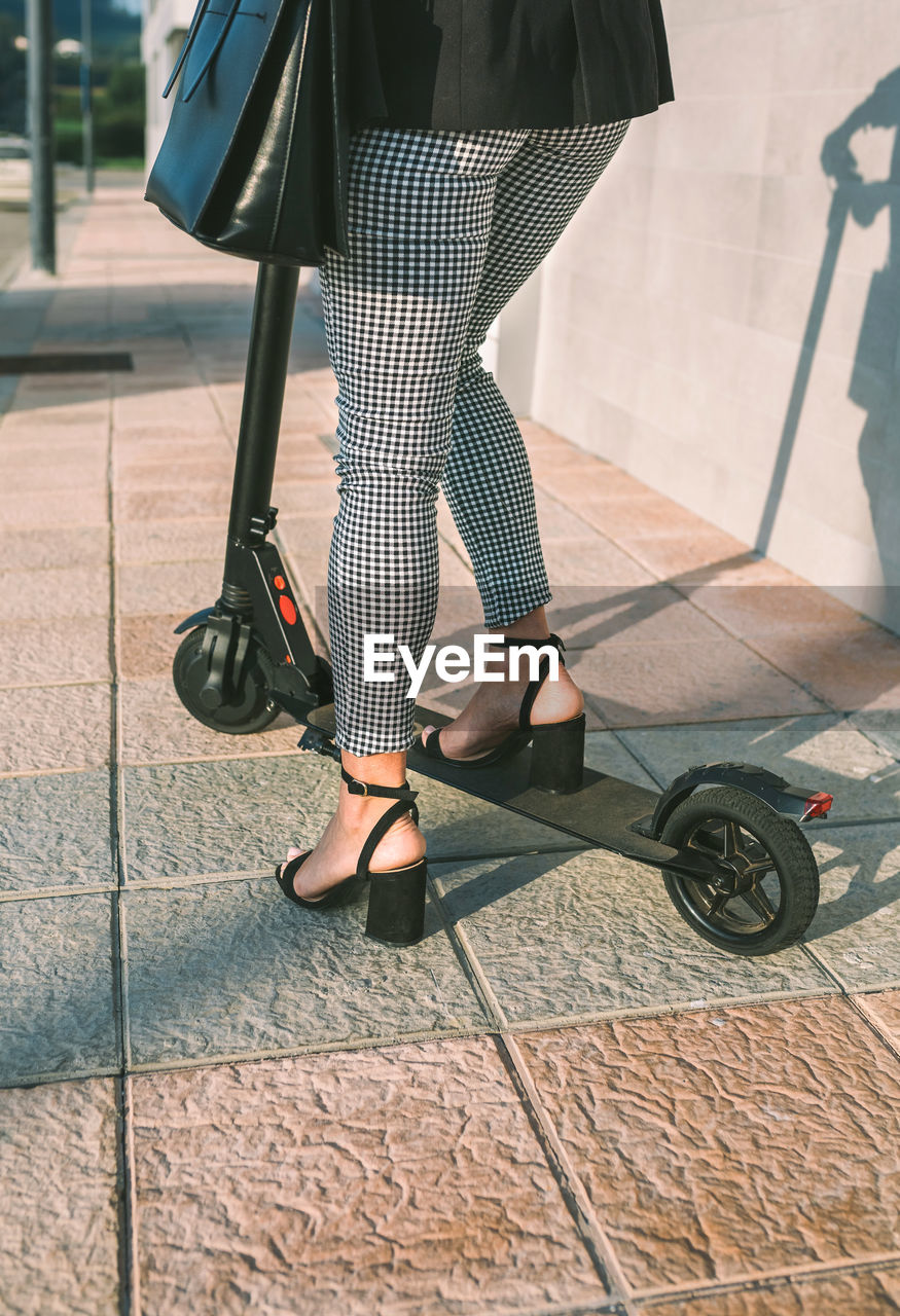 Low section of businesswoman riding electric push scooter on sidewalk