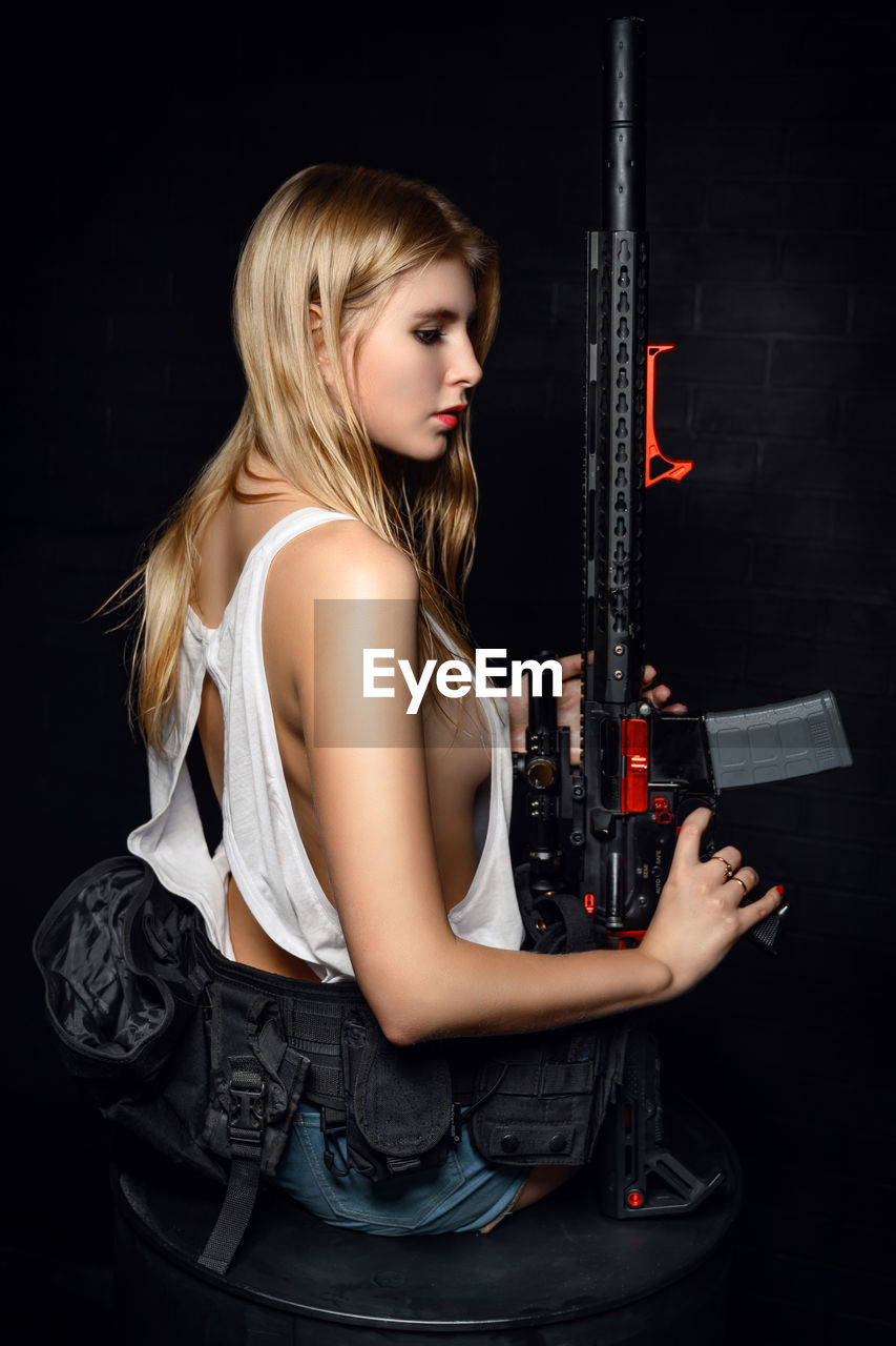 Young woman holding rifle against black background