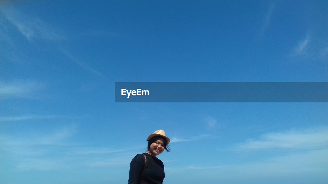 Low angle view of teenage girl standing against blue sky