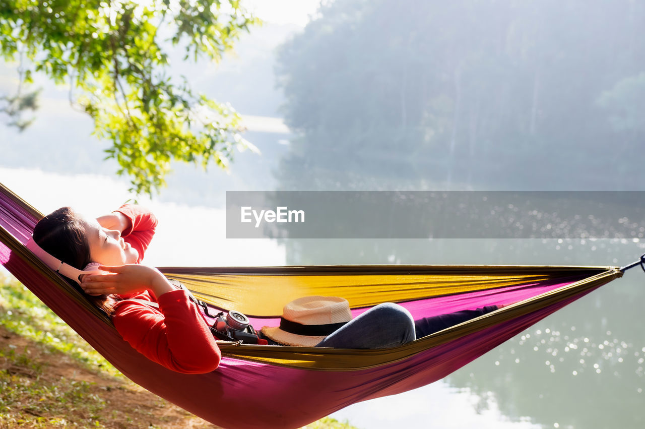 Woman happily listening to music in a hammock in a park, pang oung, mae hong son province, thailand.