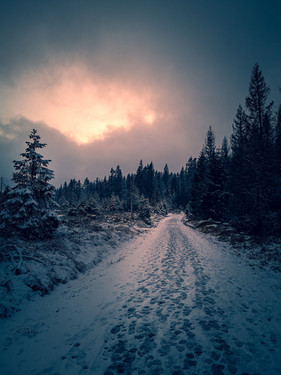 Snow covered land against sky during sunset