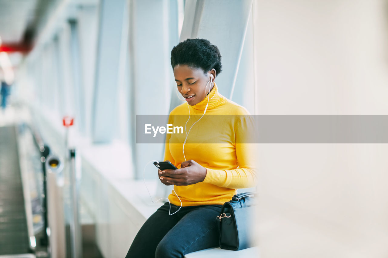 Attractive african girl is waiting for a train in the subway and listening to music with headphones.