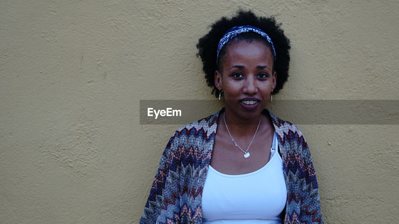 Portrait of smiling young woman standing against wall