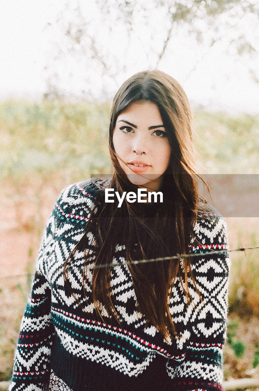 YOUNG WOMAN LOOKING AWAY WHILE STANDING ON WOODEN WALL