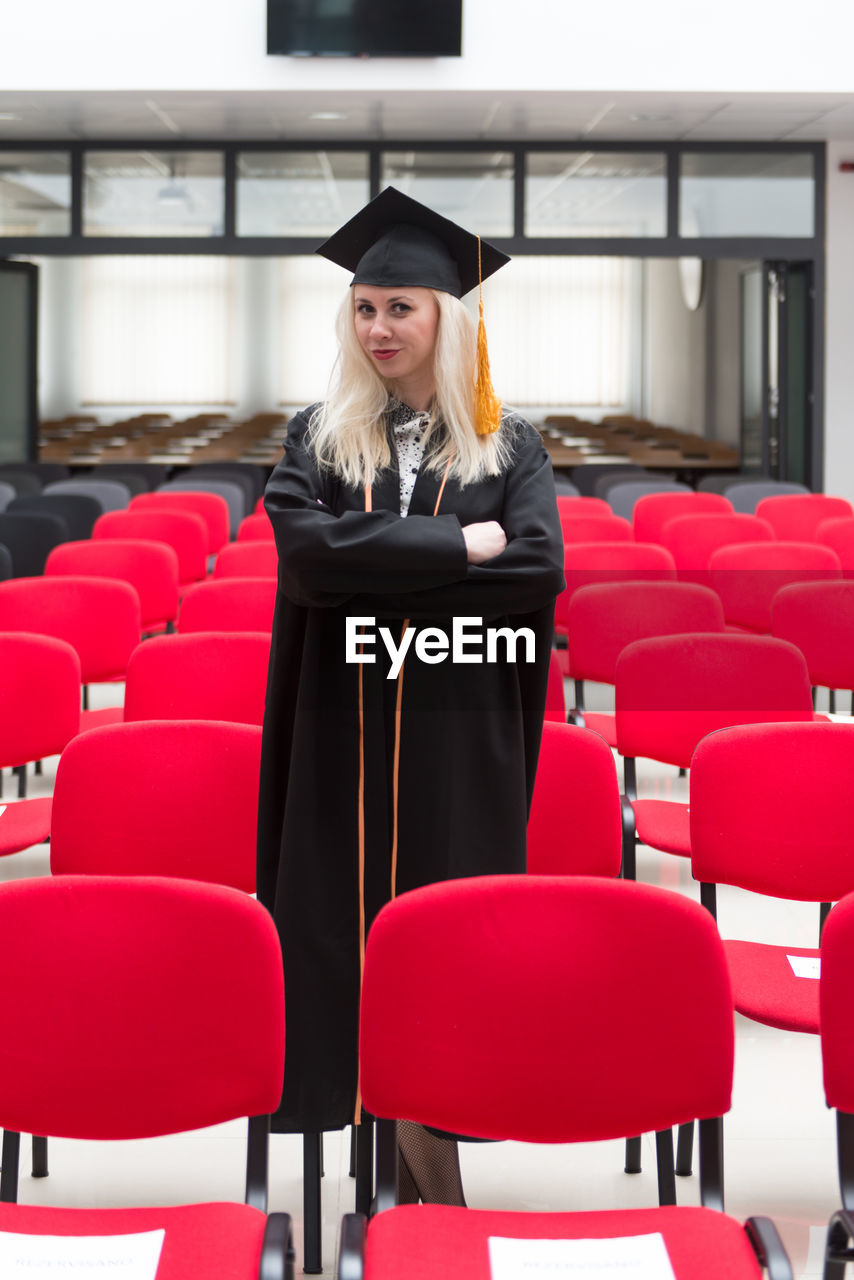 Female blonde college or high school graduate confidently wearing black cap and gown at graduation