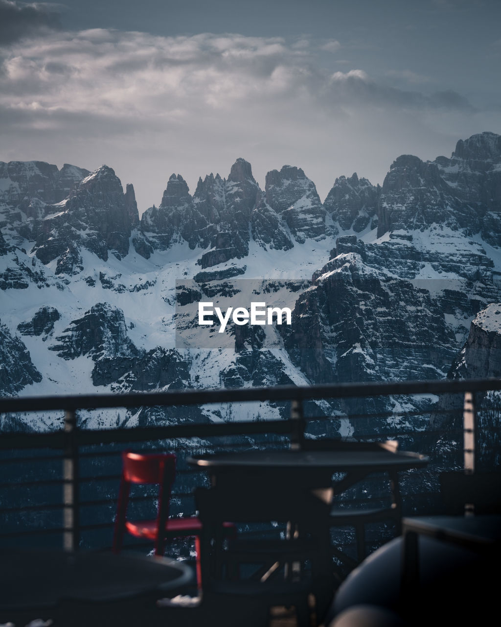 Close-up of chair by railing against snowcapped mountain