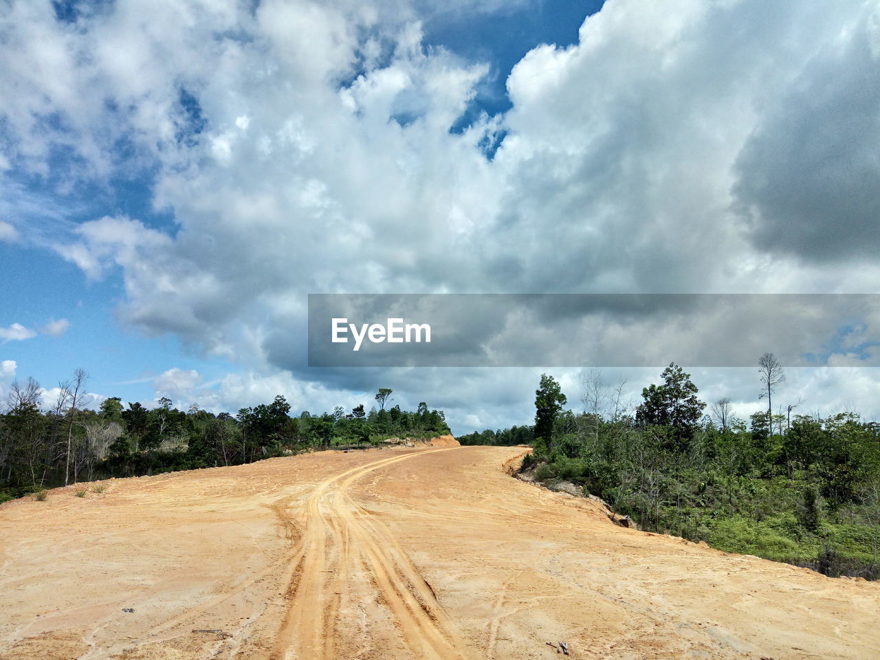 Dirt road amidst field against sky