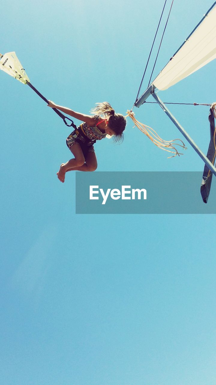 Low angle view of girl jumping in bungee trampoline against blue sky