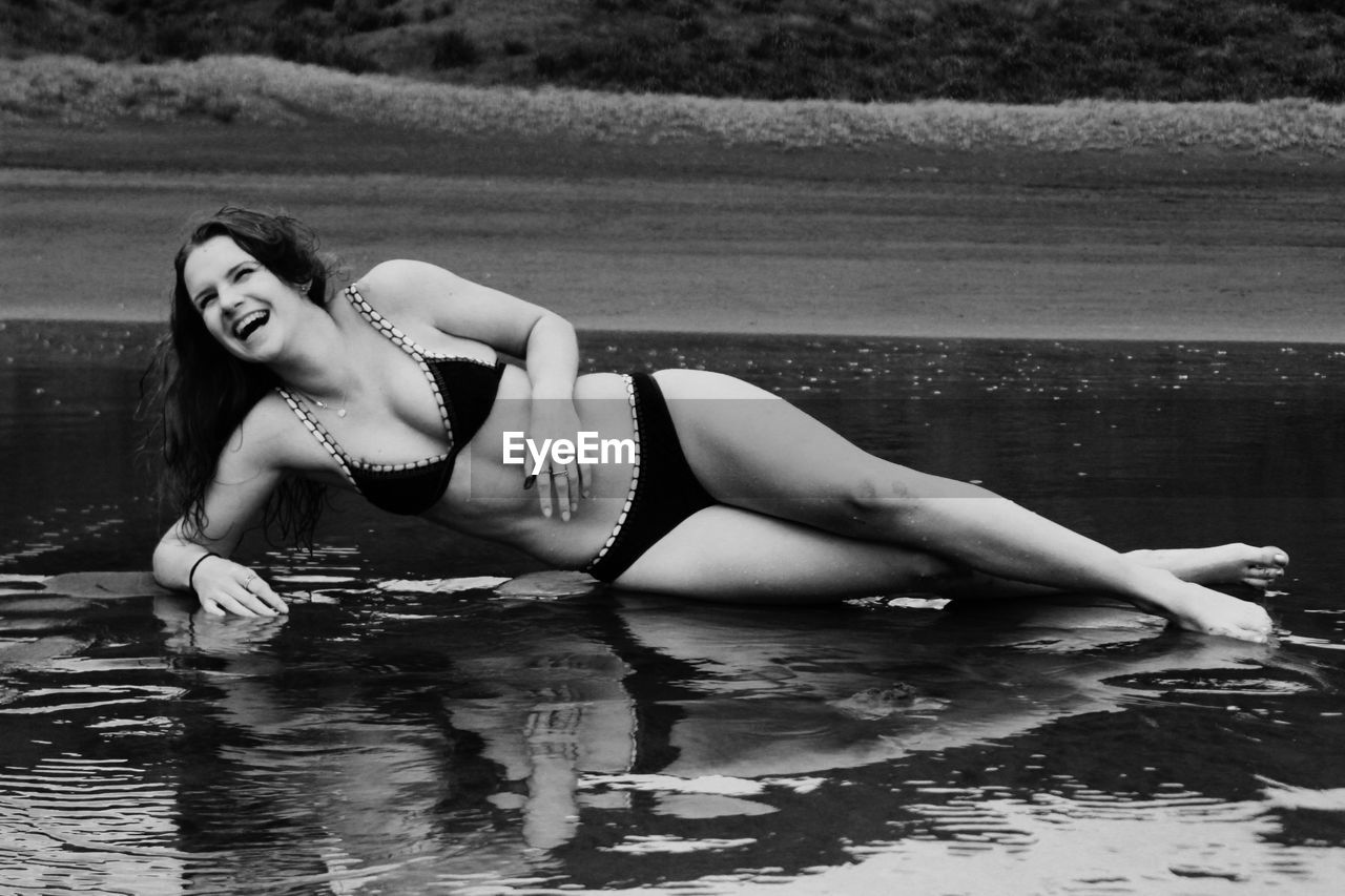 Happy teenage girl in bikini lying on shore at beach