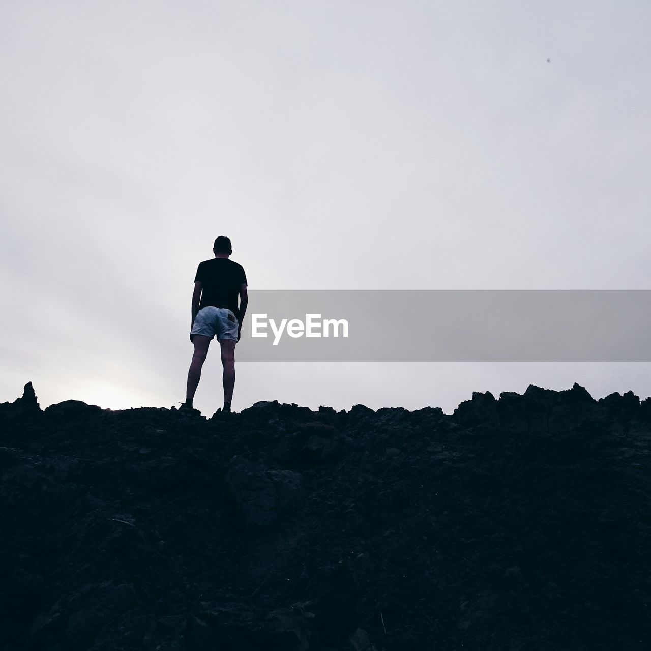 Rear view of man standing on rocks against sky