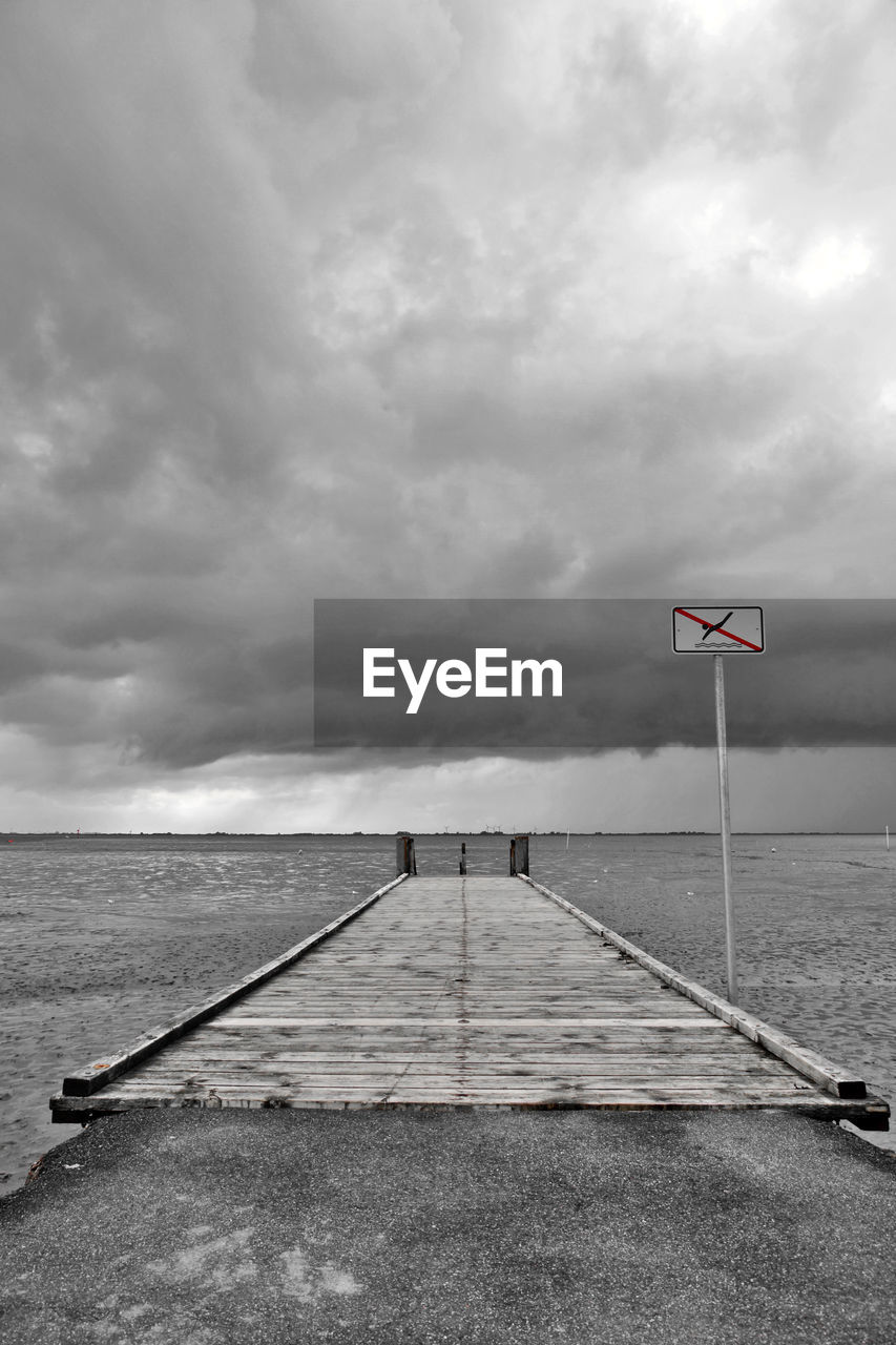 No swimming sign on pier by sea against cloudy sky