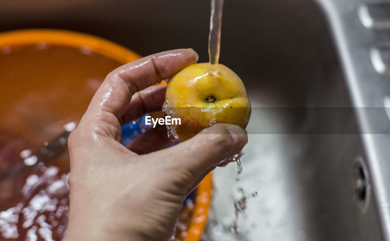 Cropped image of person hand holding apple over running water in sink