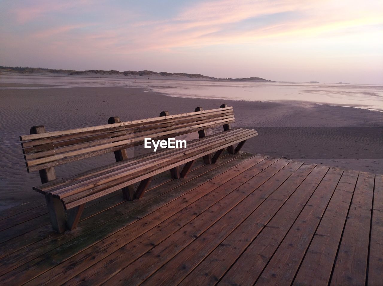 Empty bench by sea against sky during sunset