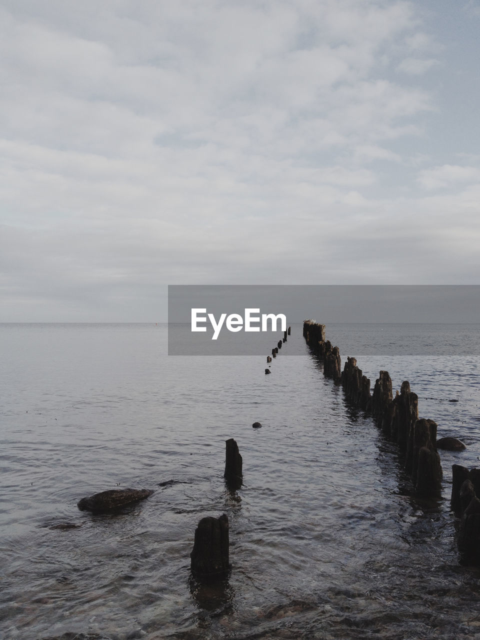 Wooden posts in sea against cloudy sky