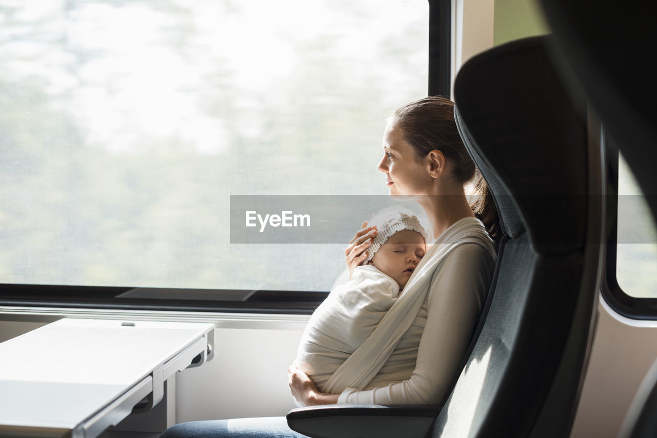 Mother with baby girl traveling by train looking out of window