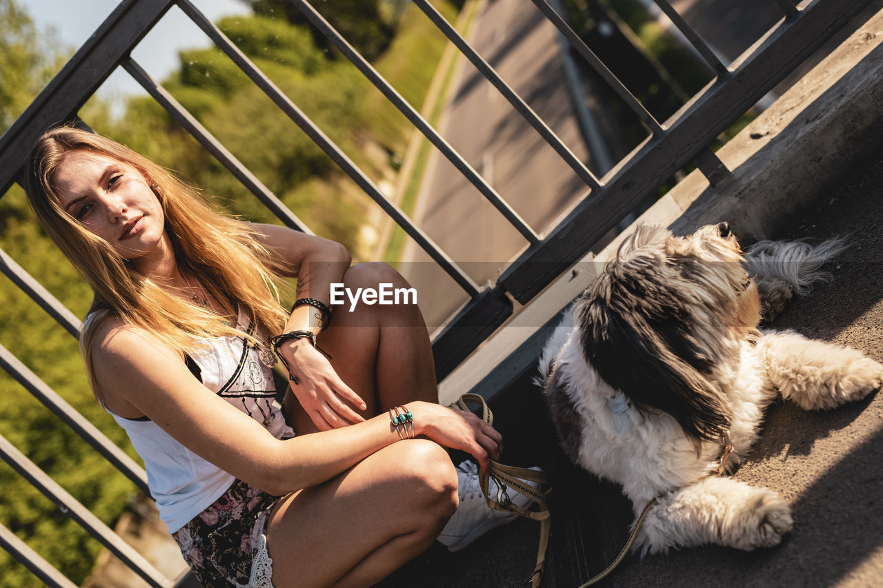 Portrait of young woman crouching by dog on footbridge