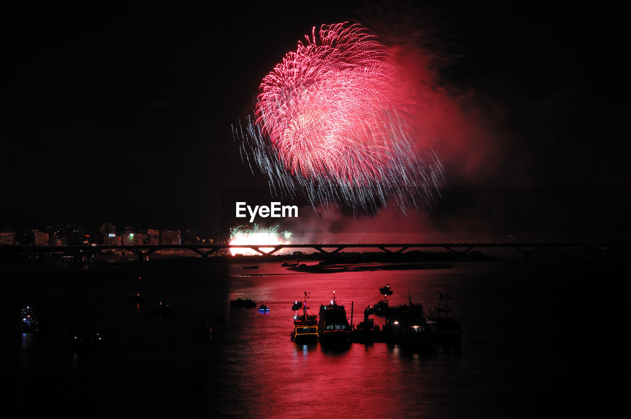 FIREWORK DISPLAY OVER ILLUMINATED FIREWORKS AGAINST SKY AT NIGHT