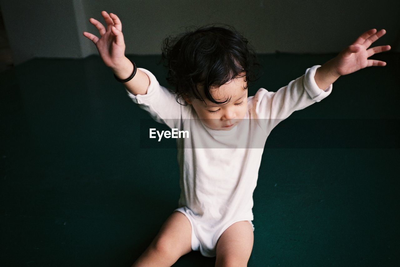 High angle view of baby girl with arms raised sitting on floor at home