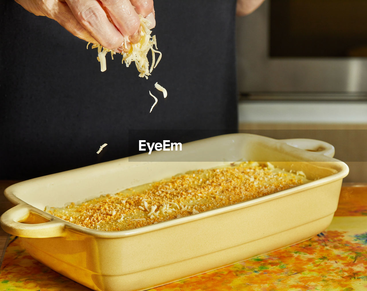 Chef pours parmesan over mashed potatoes over fried minced meat with onions and carrots in ceramic