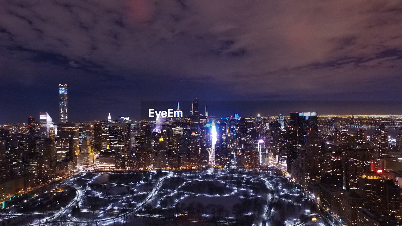 Illuminated buildings against cloudy sky at night