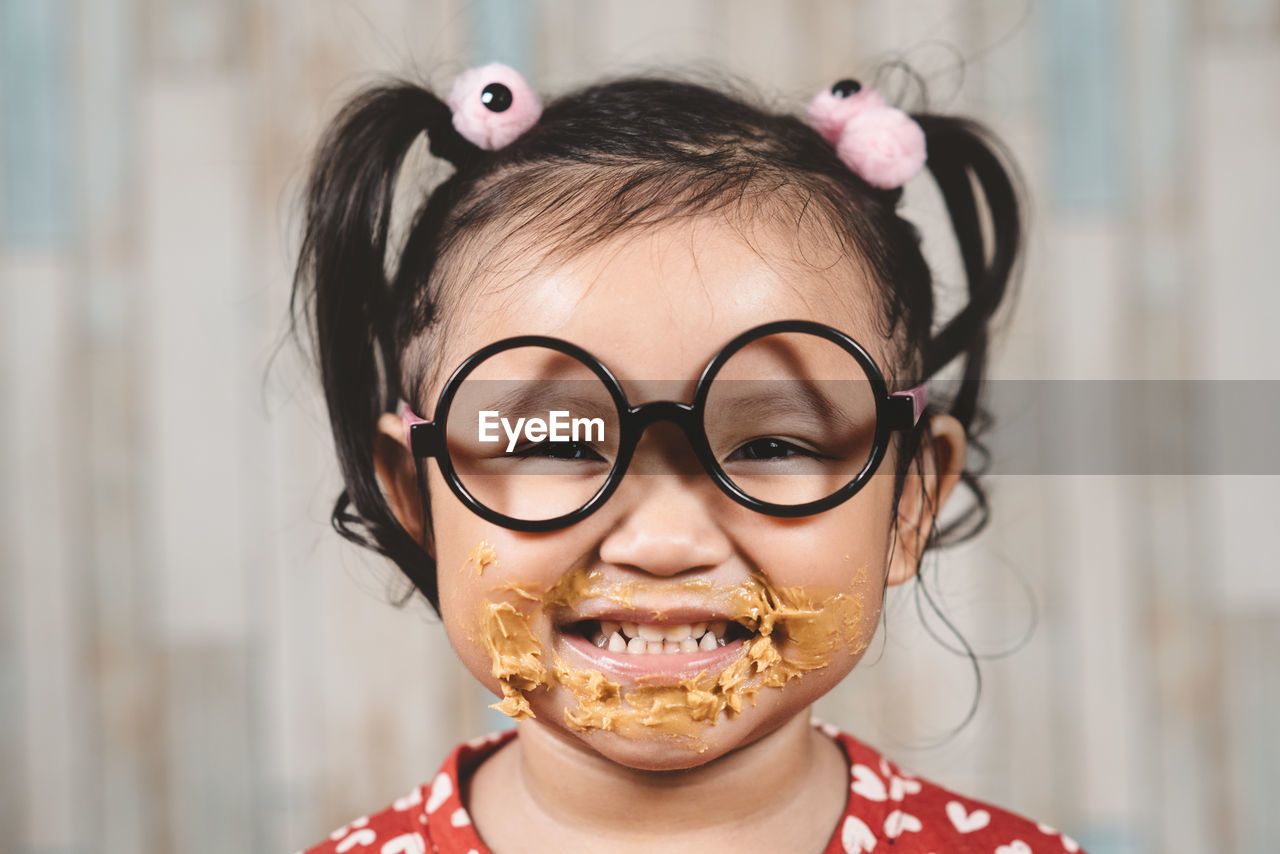 Close-up portrait of messy girl eating peanut butter against wall