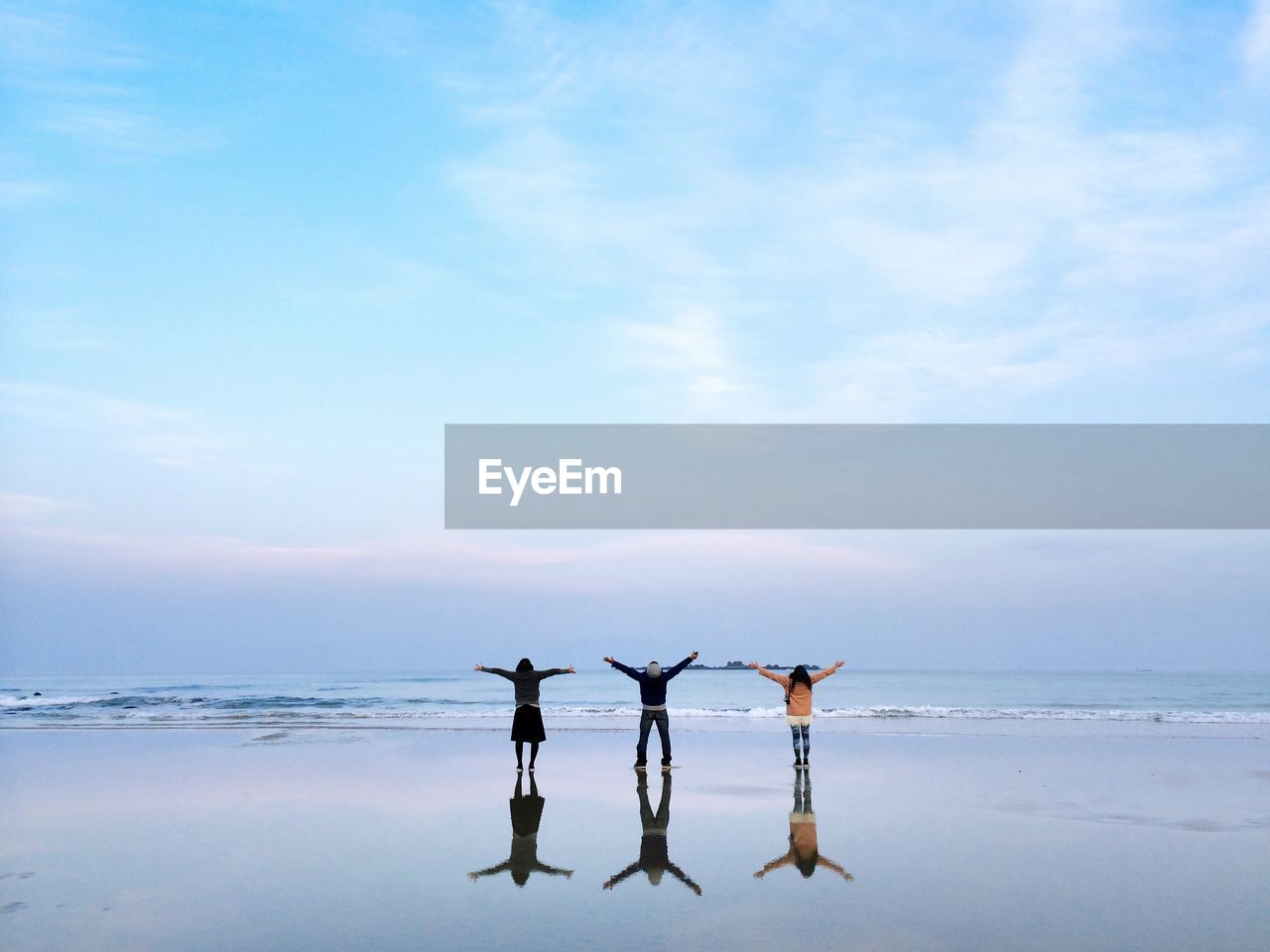 Rear view of people on wet beach by sea against sky