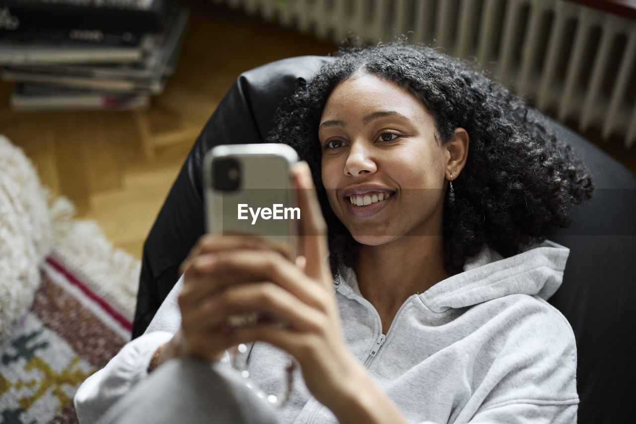 Smiling young woman lying on bean bag and using phone