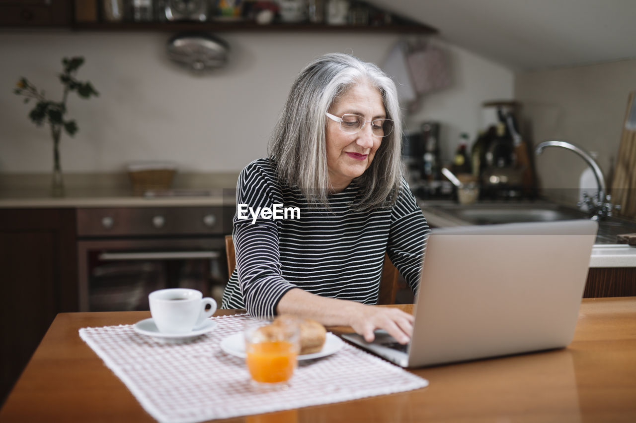 Portrait of senior woman using laptop at breakfast table