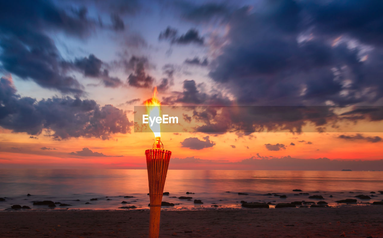 Scenic view of sea and a torch against sky during sunset