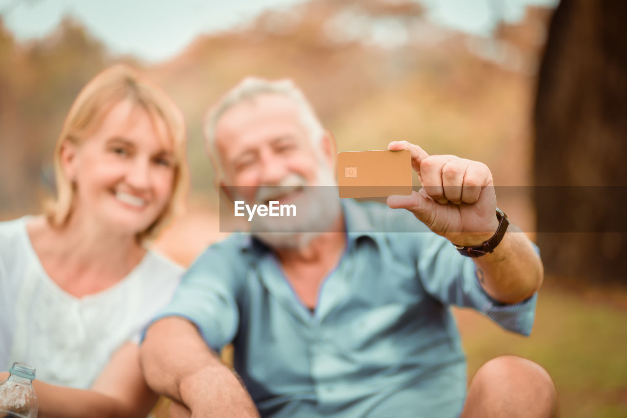 Portrait of smiling couple holding credit card while sitting in park