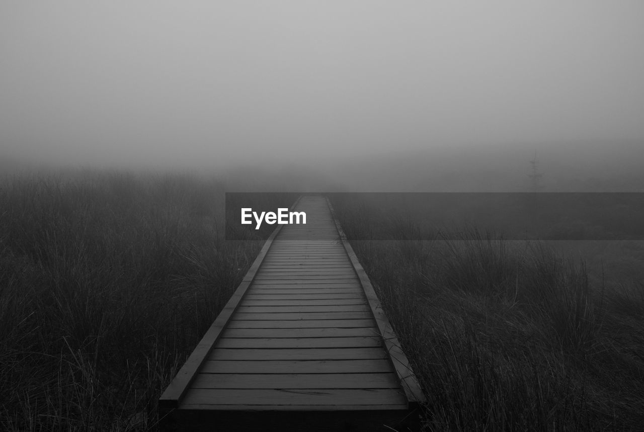 Boardwalk on landscape in foggy weather