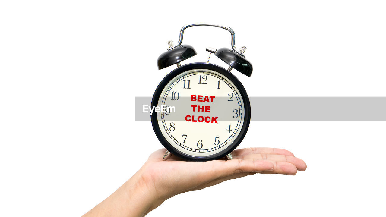 Cropped hand of woman holding clock over white background