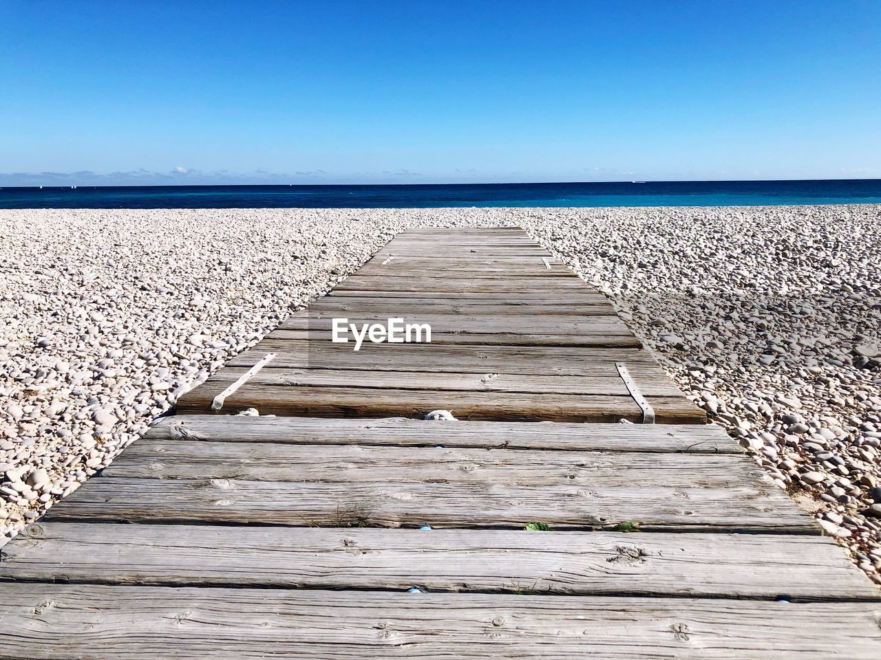 BOARDWALK LEADING TO SEA AGAINST CLEAR SKY