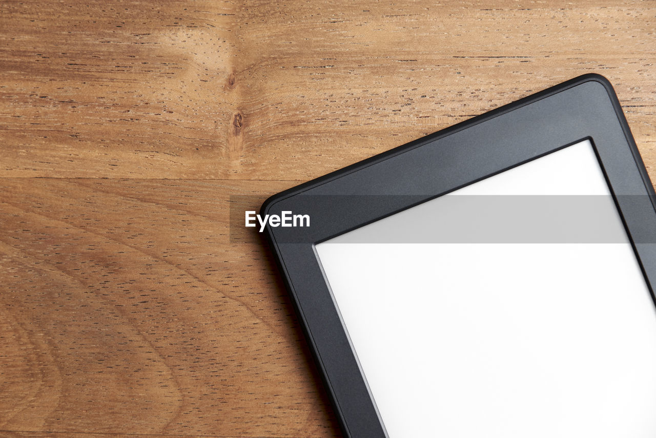 Closeup image of an electronic reader with blank screen on a wood surface. technology and modernity.