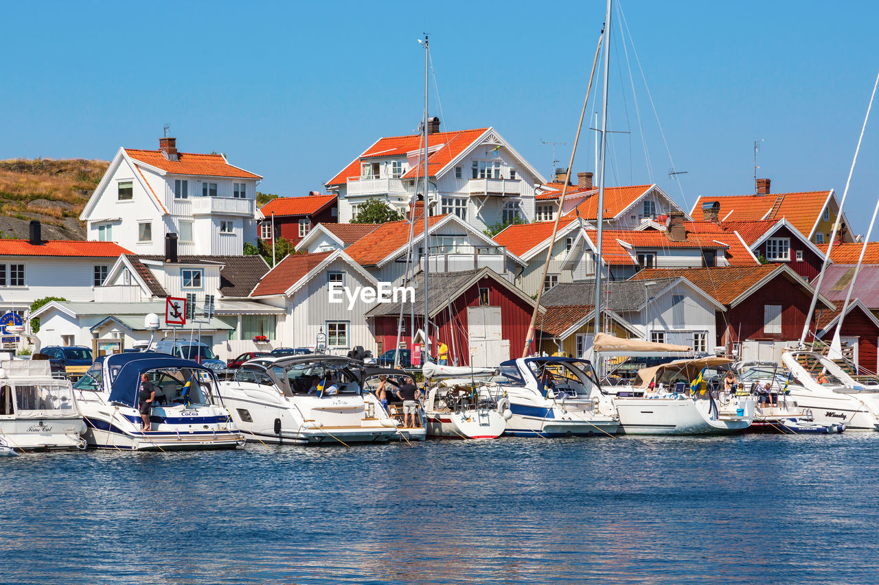 Sailboats moored on sea by buildings against clear sky