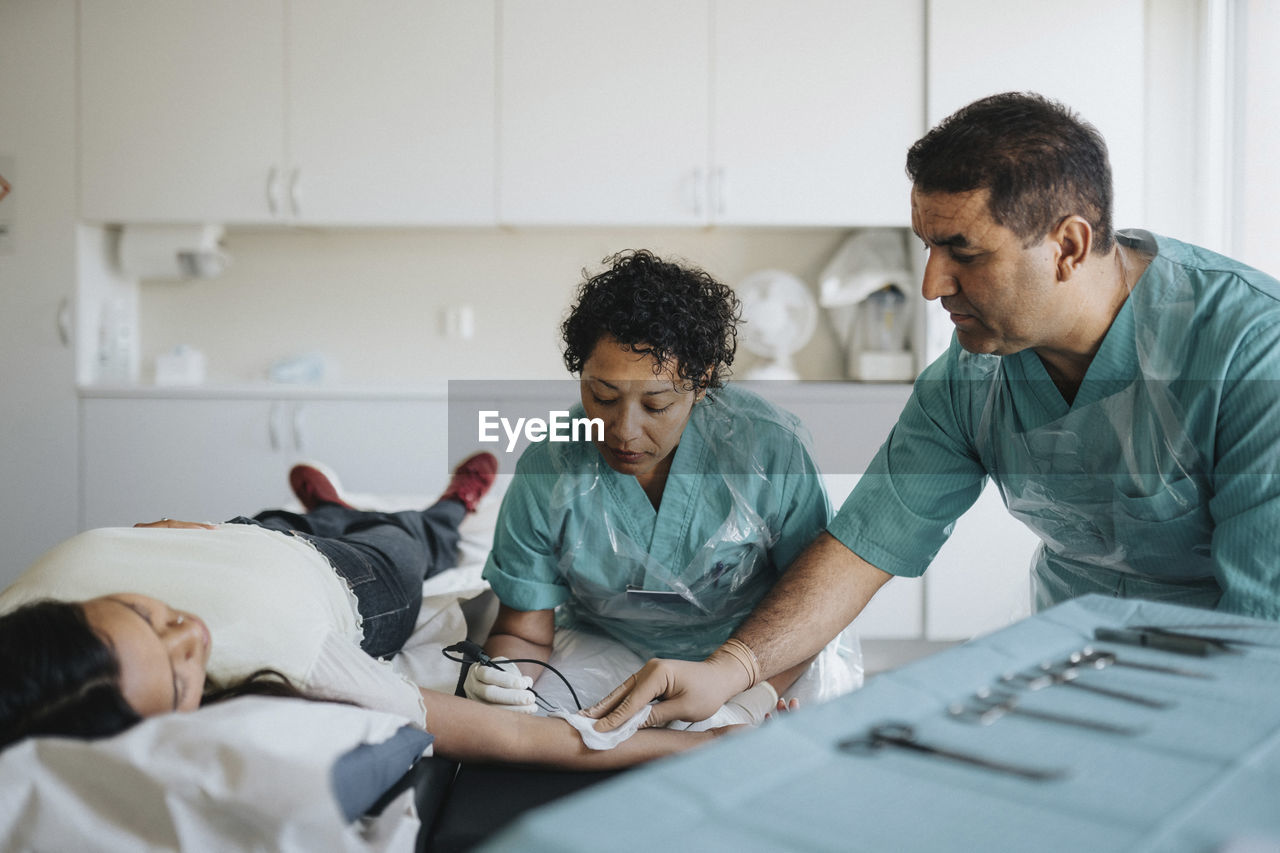 Male and female surgeons operating young woman lying on examination table in hospital