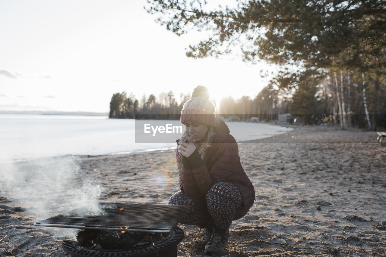 Woman warming up by a fire at the beach in winter in sweden