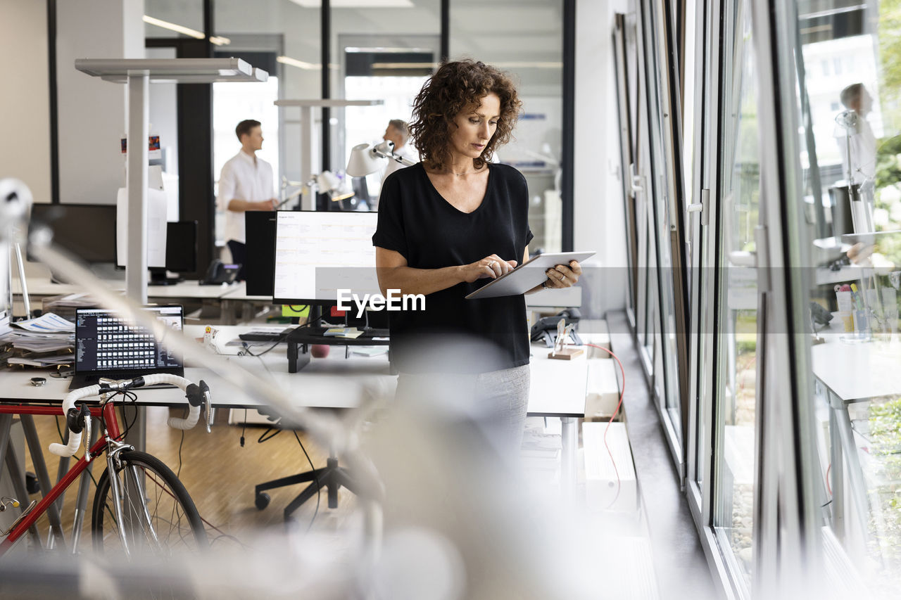 Businesswoman using digital tablet while working with colleague in background at open plan office