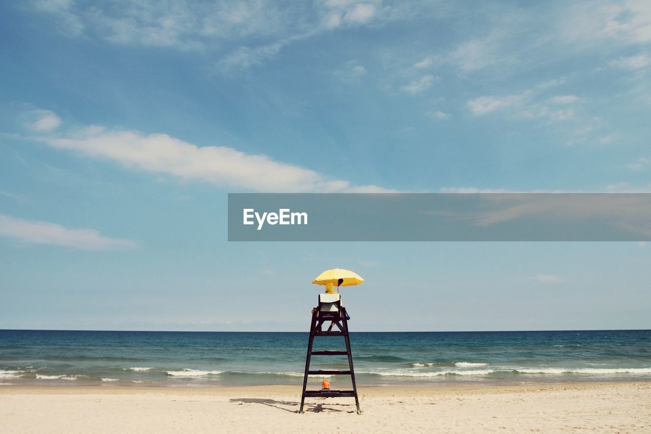 Lifeguard sitting on chair at beach against sky