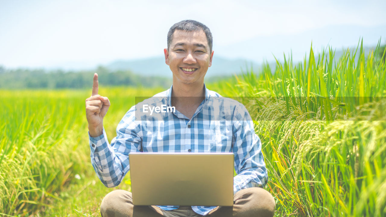 Portrait of smiling man holding laptop in field