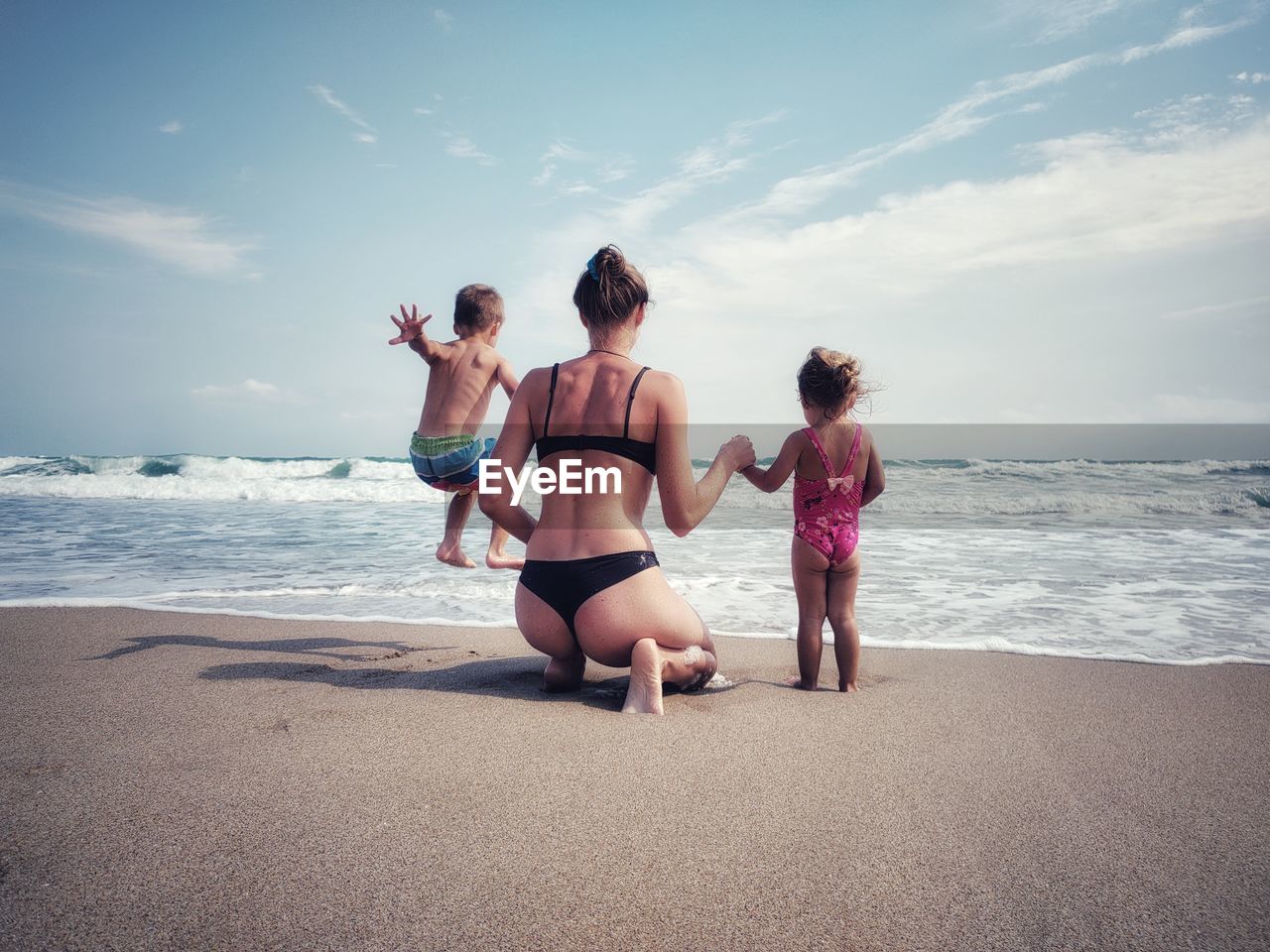 rear view of mother and daughter at beach against sky