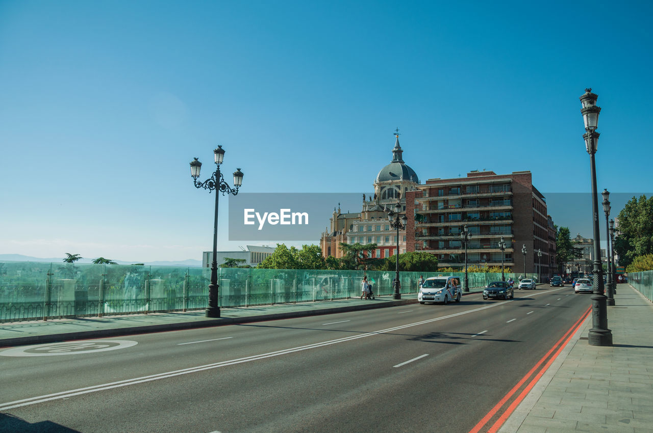 Almudena cathedral dome behind buildings on street with light posts in madrid, spain.