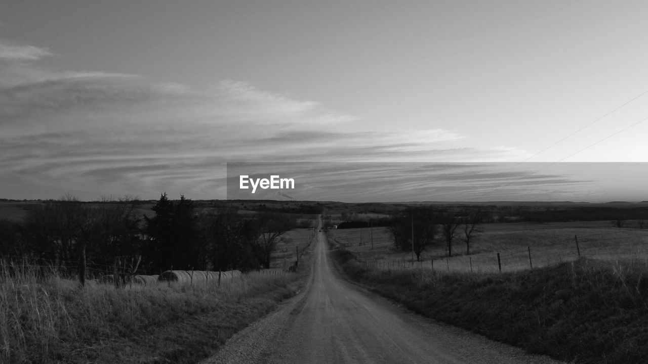 Empty road amidst field against sky