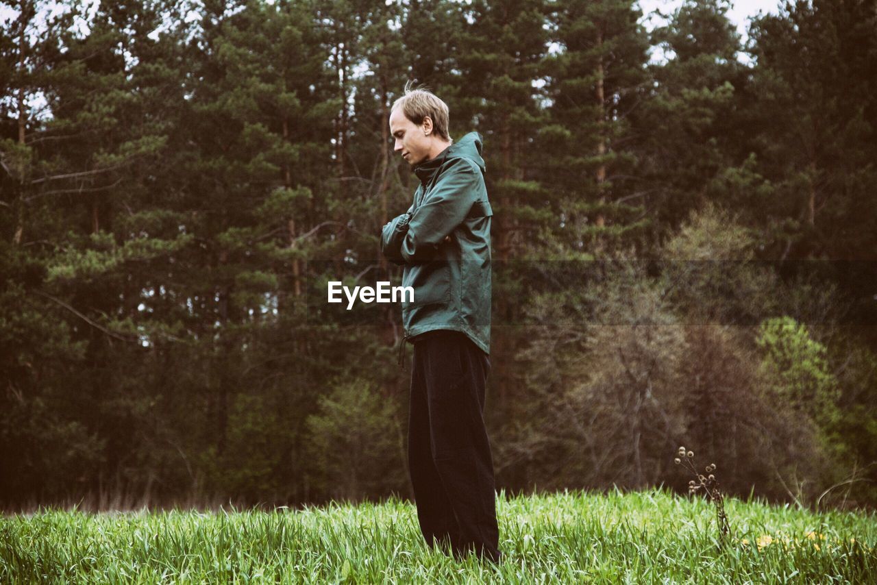 Side view of man standing on grassy field in forest