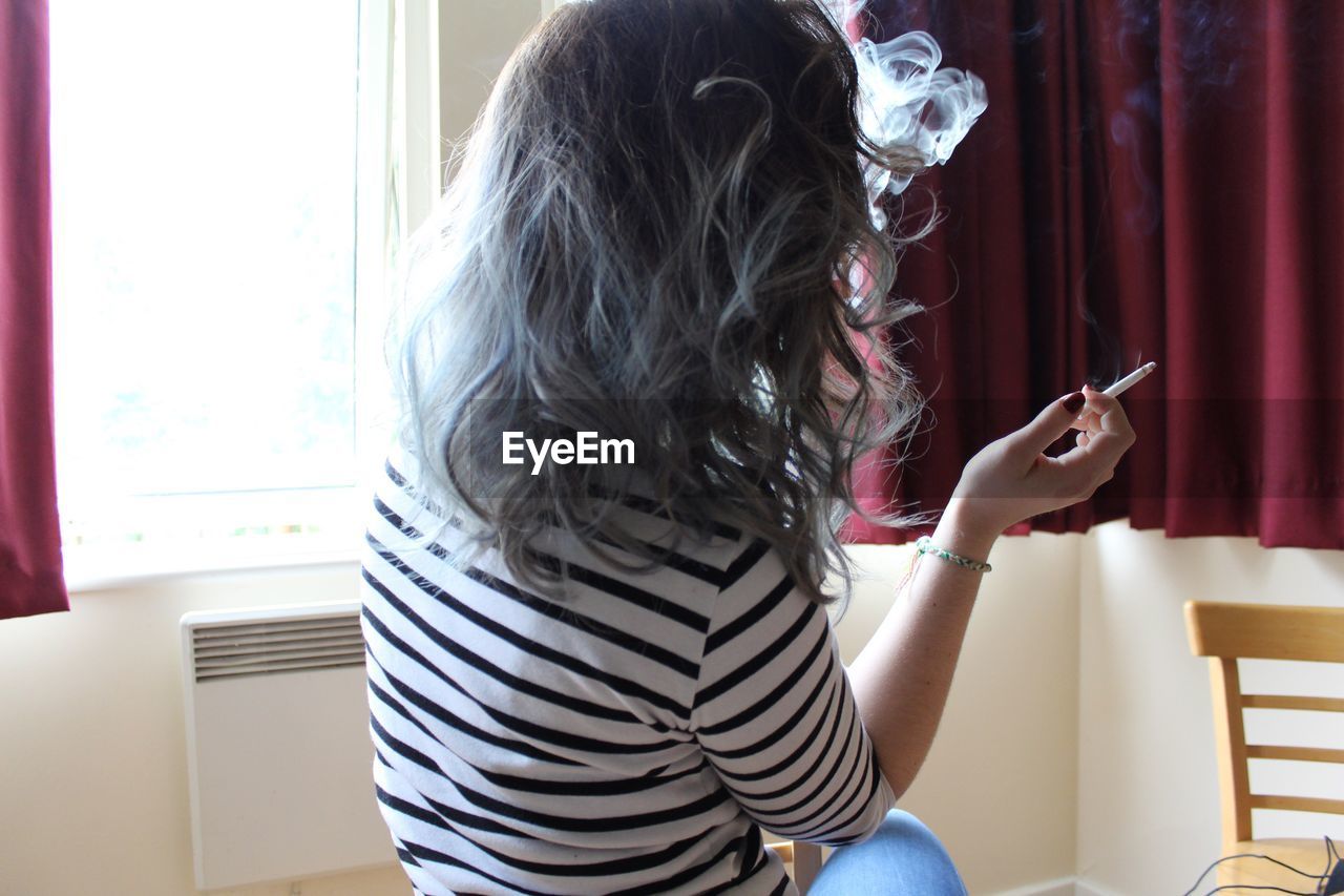 Rear view of woman smoking cigarette in room