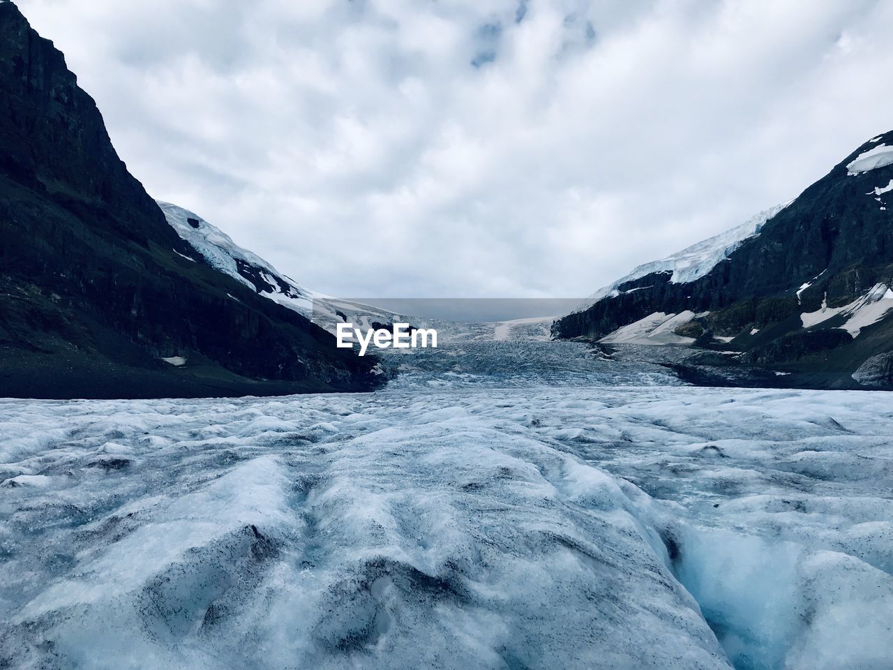 Scenic view of glacier amidst rock formation against cloudy sky